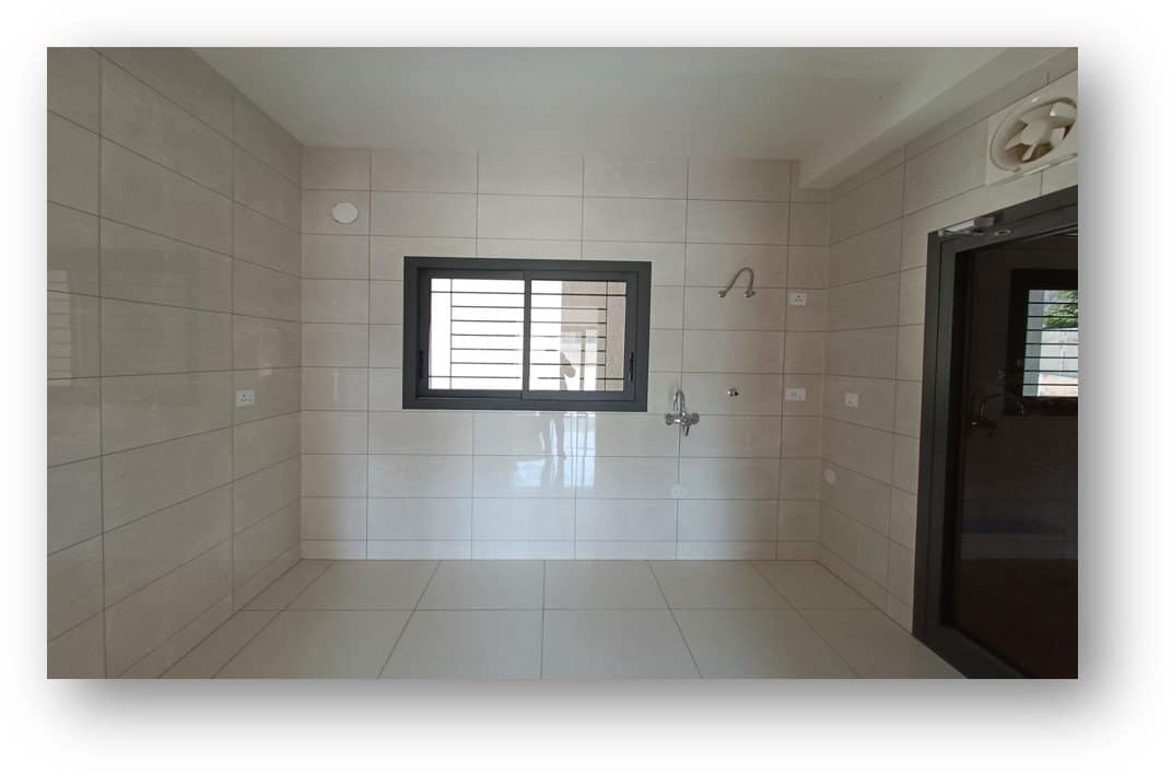 Bare shell bathroom or utility area, featuring light-colored tiles on walls and floor, a sliding window with grills, plumbing fixtures, and an exhaust fan, poised for complete interior transformation by Olangana Design in Bangalore.