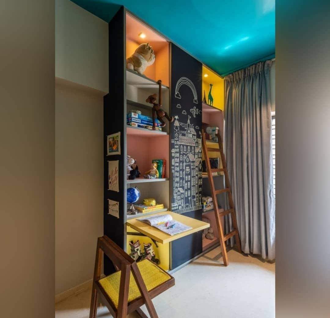 Modern children's room interior featuring a custom black and colorful (yellow, pink) shelving unit with an integrated study desk, chalkboard wall art, and a wooden ladder, expertly designed by Olangana Design in Bangalore.