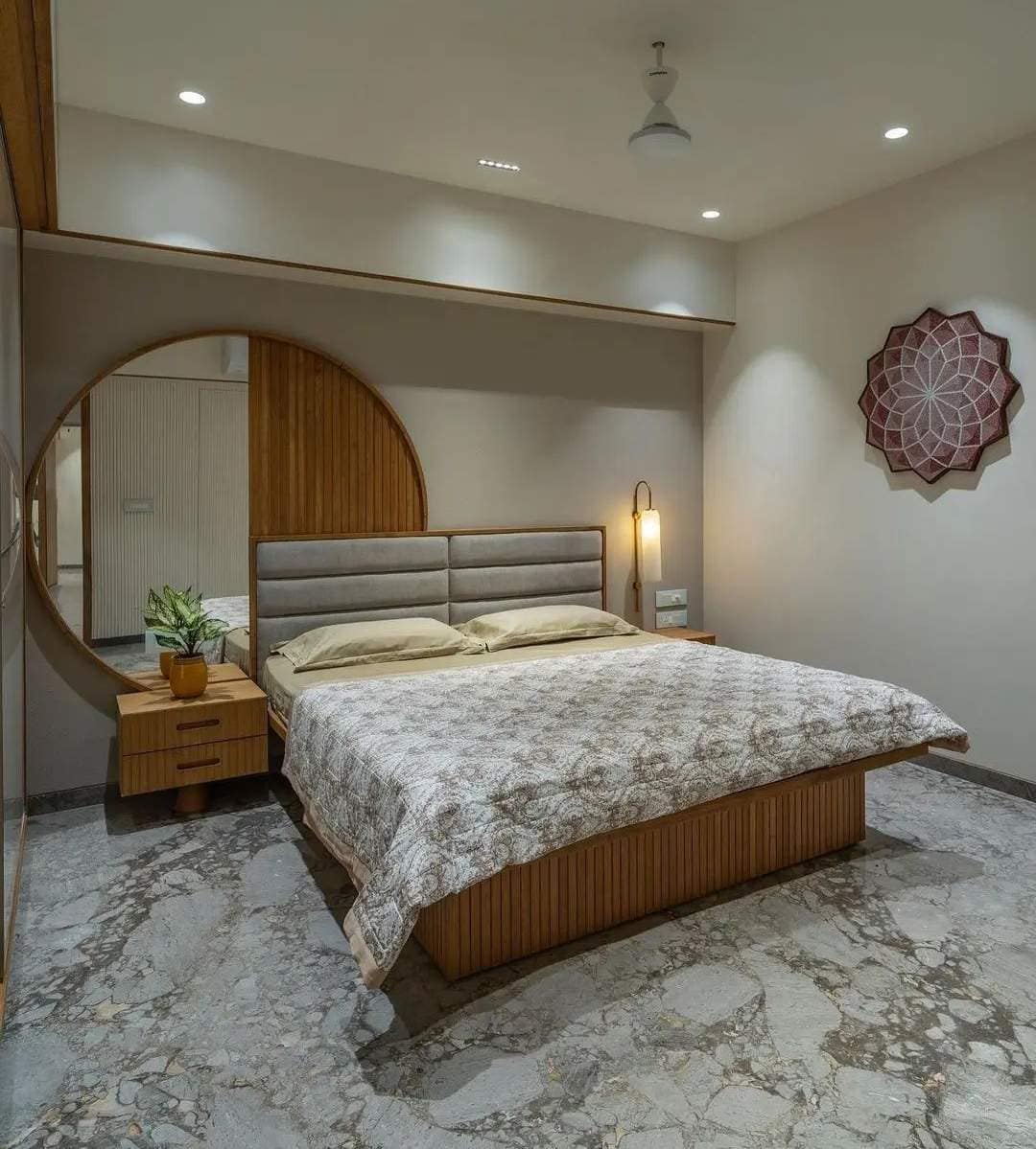Modern bedroom interior design by Olangana Design in Bangalore featuring a wooden slatted bed, grey padded headboard, round mirror, and sophisticated marble flooring.