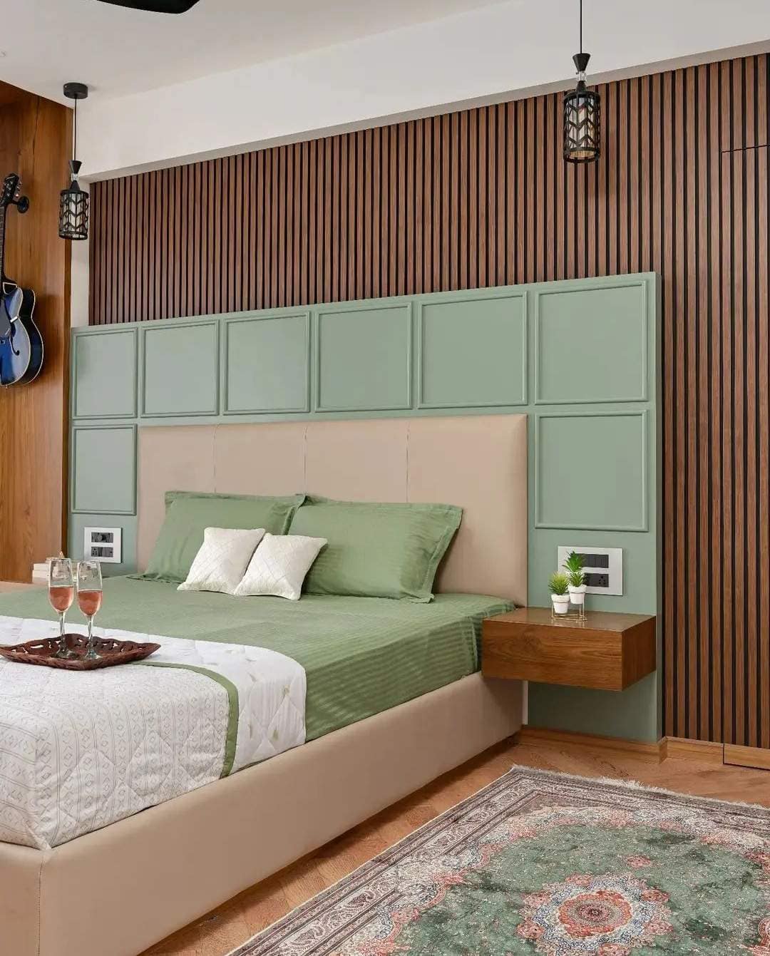 Modern bedroom interior designed by Olangana Design in Bangalore, showcasing a beige upholstered bed with sage green bedding, a distinctive green panel headboard, and warm wood slatted wall paneling for a serene aesthetic.