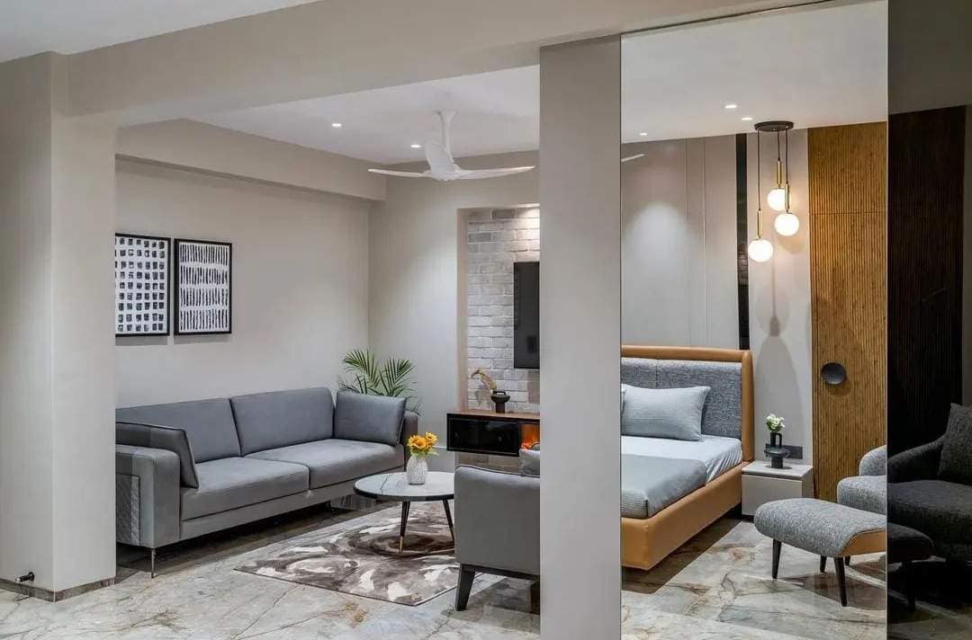 Modern open-plan living and bedroom interior design by Olangana Design in Bangalore, featuring a grey sofa, contemporary bed, and elegant lighting.