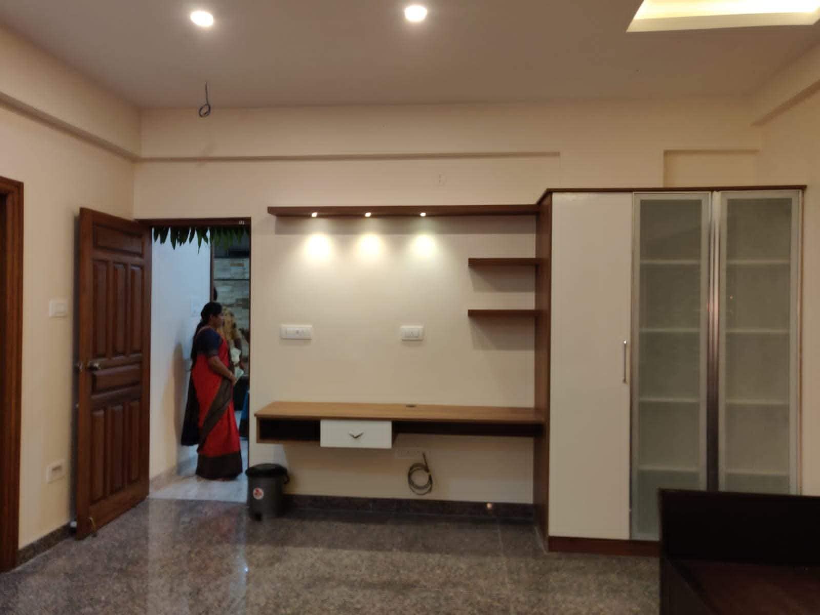 Modern living room interior design with custom TV unit, integrated storage, and display cabinets by Olangana Design in Bangalore, featuring sleek wood and white finishes, ambient lighting, and elegant granite flooring.