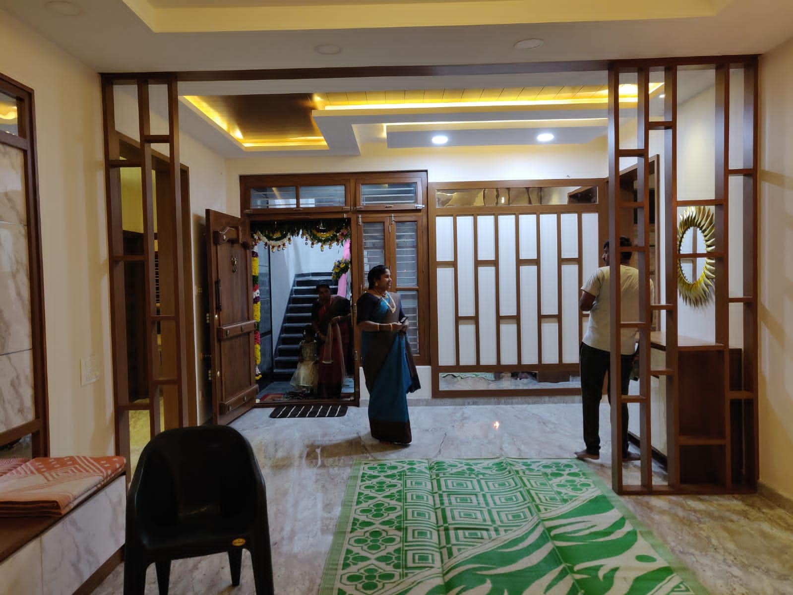 Elegant modern Indian entryway interior design by Olangana in Bangalore, featuring intricate wooden partition walls, warm ambient lighting, and a stylish sunburst mirror.