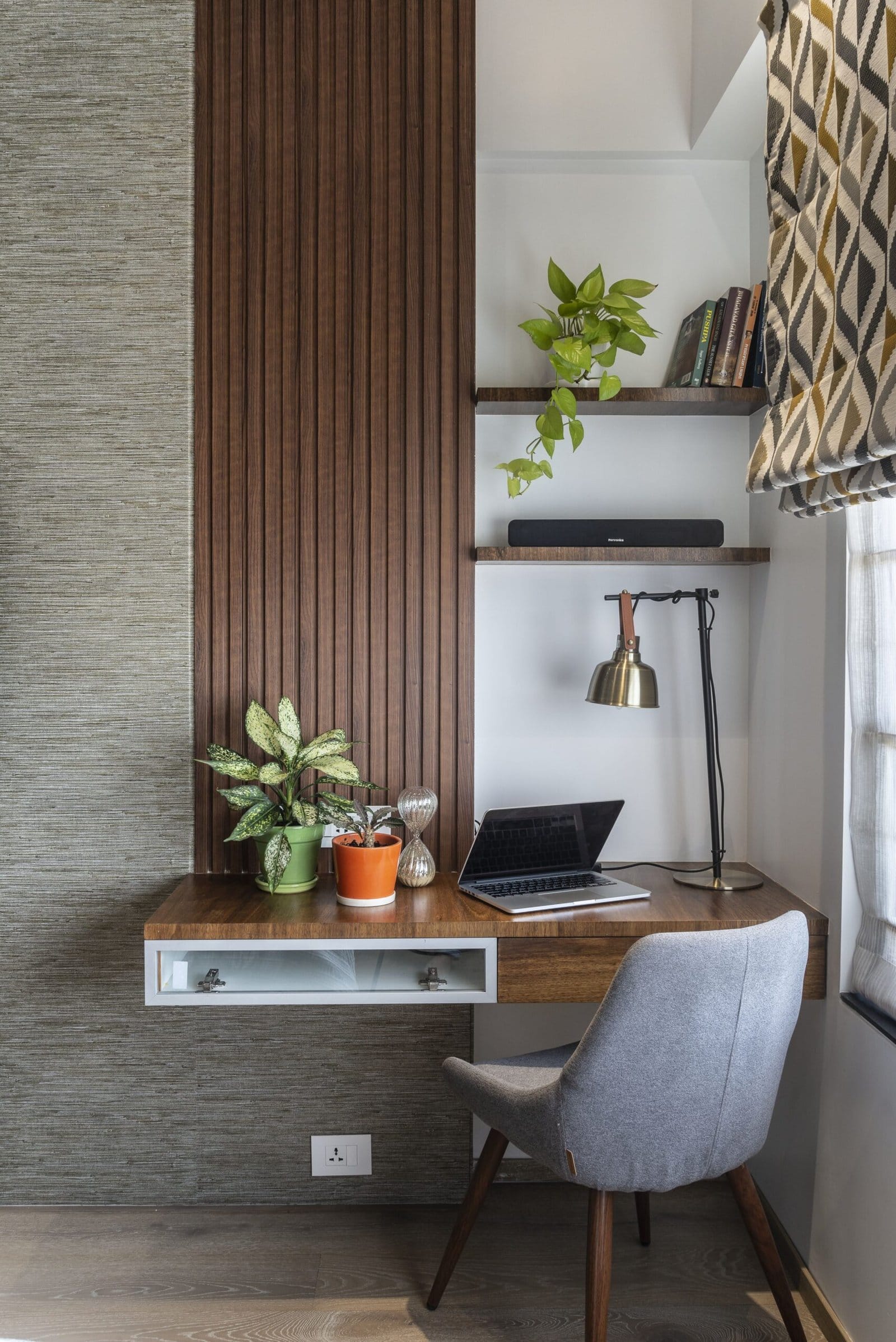 Modern home office interior design by Olangana in Bangalore, featuring a floating wooden desk, a comfortable grey chair, and natural plant decor.
