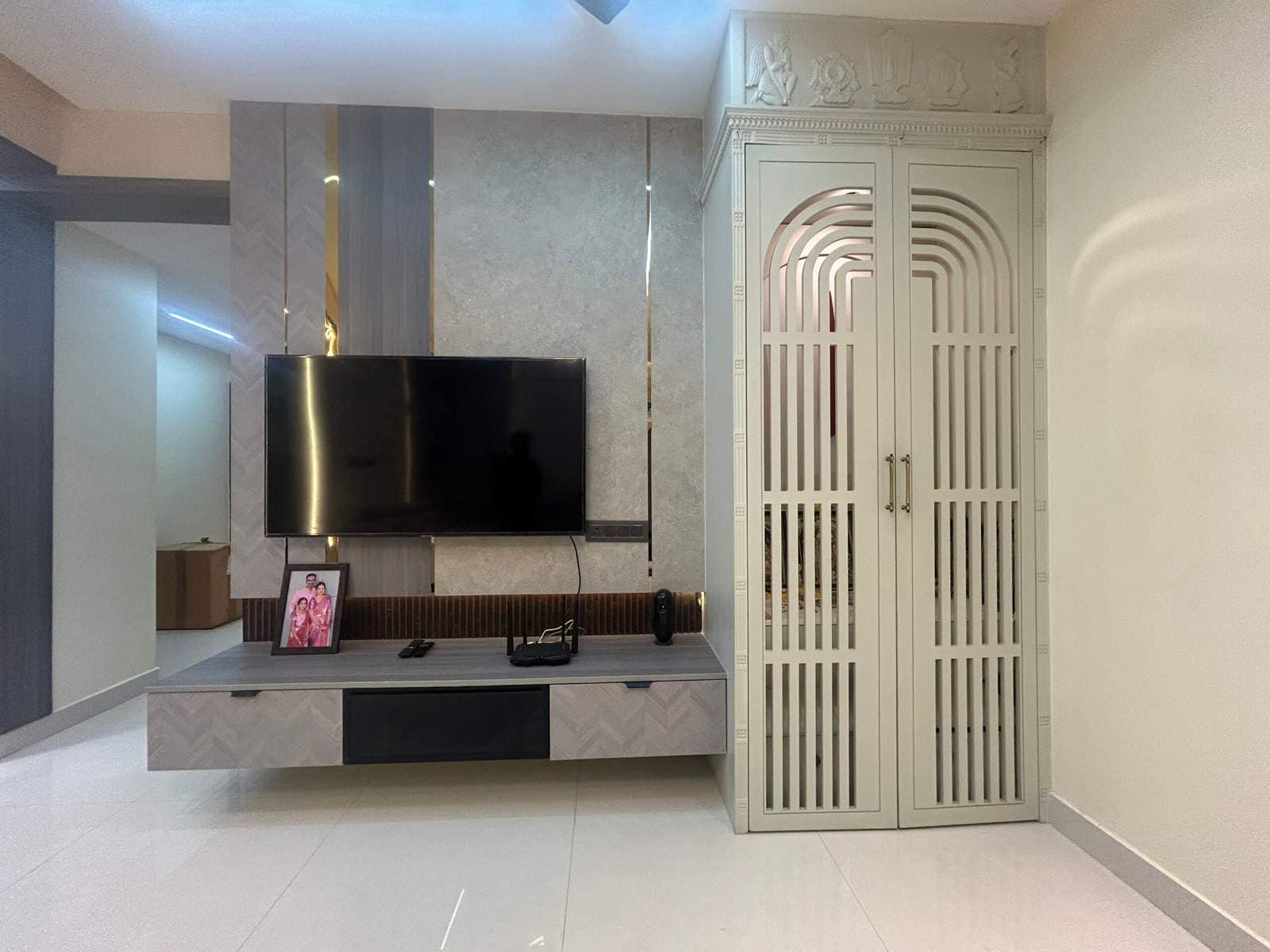 Elegant pooja room with enclosed doors in living hall beside TV cabinet in Bangalore home by Olangana Design’s.