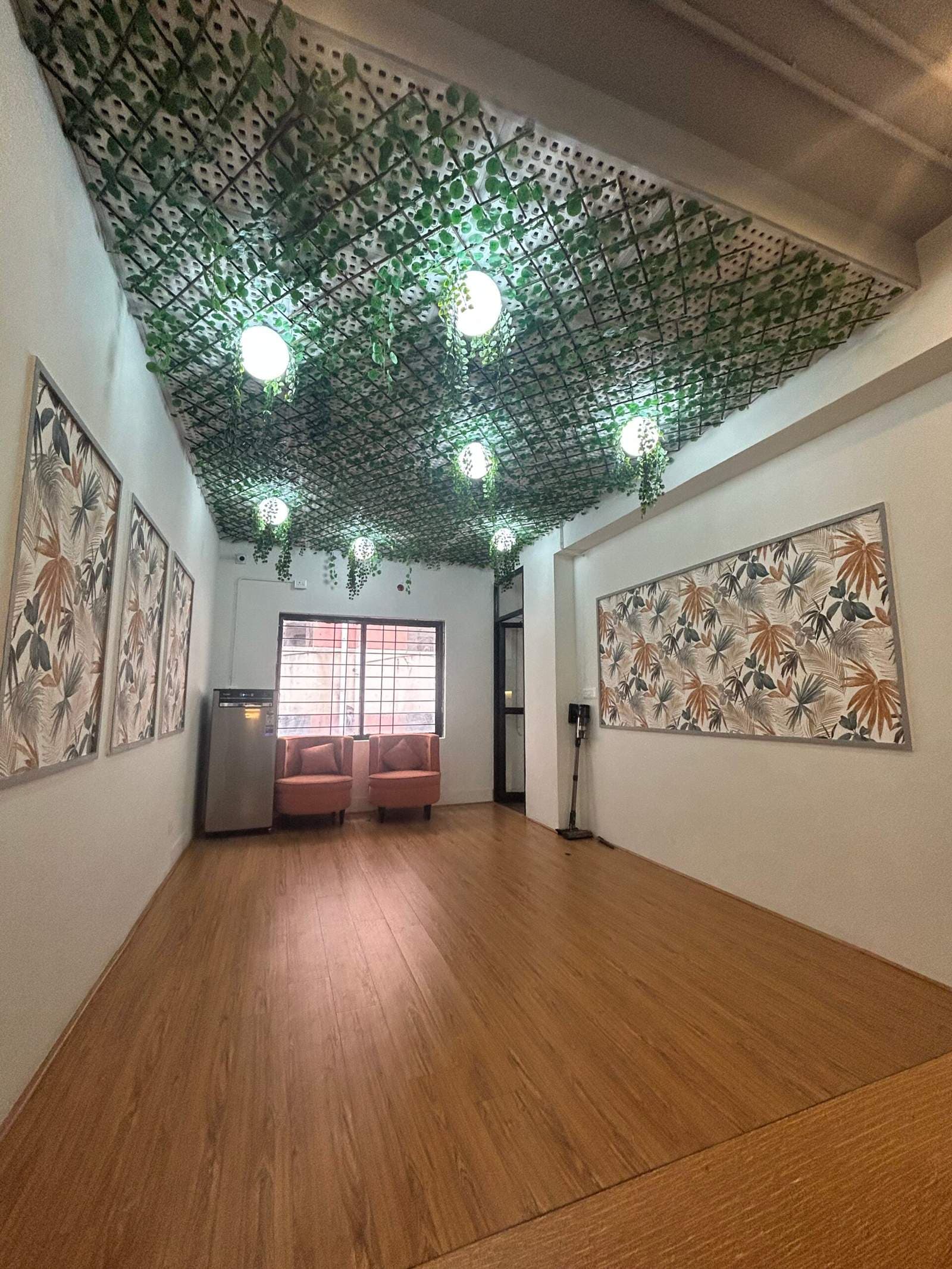Nature inspired office lounge interior in Bangalore with green ceiling vines, warm wooden flooring, and modern seating by Olangana Designs