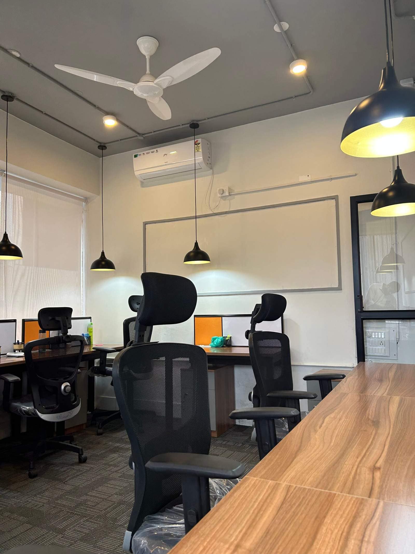 Olangana Design’s presents a modern corporate office cabin interior in Bangalore with four seating chairs, AC, ceiling fan, writing board, lamps, and a neat designer ceiling for a professional workspace.