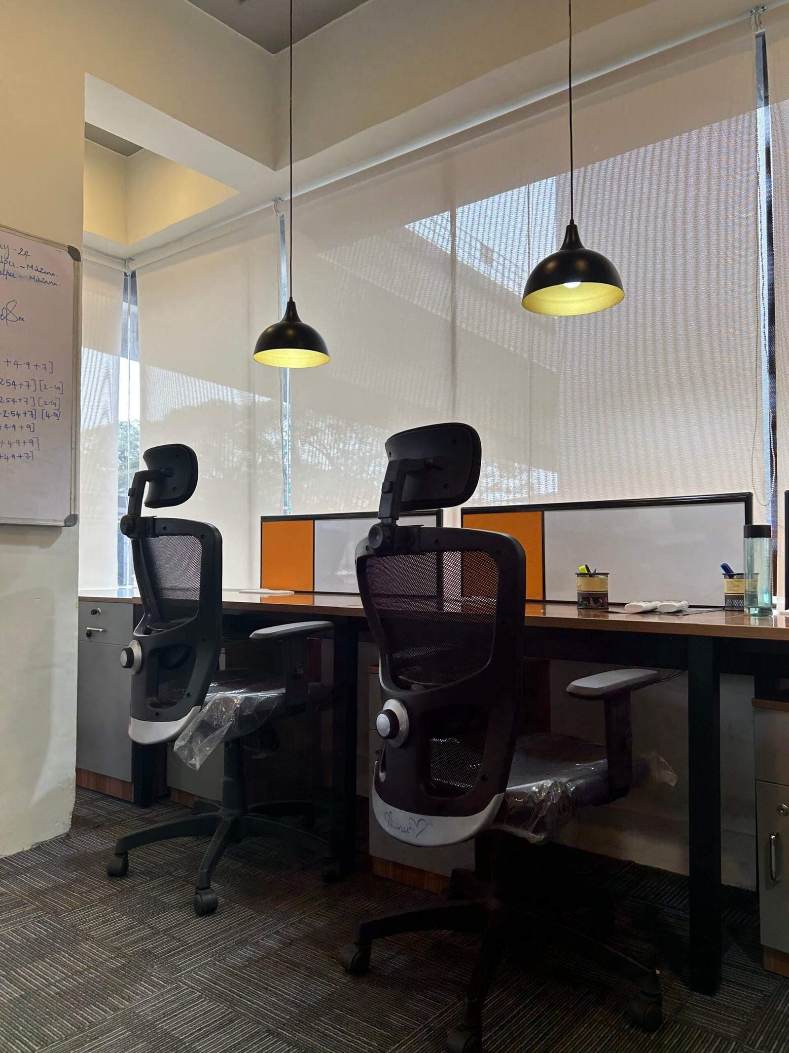 Olangana Design’s modern small corporate office cabin interior in Bangalore featuring two executive chairs, stylish desk lighting lamps, and wall board setup designed for productive workspace interiors.
