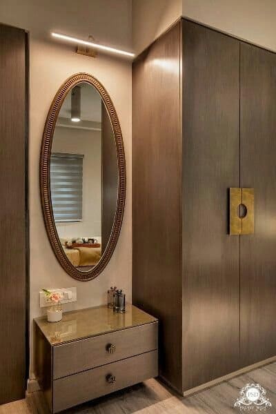 Elegant modern interior dressing area by Olangana Design in Bangalore, featuring an oval mirror, floating vanity, and dark wood wardrobes.
