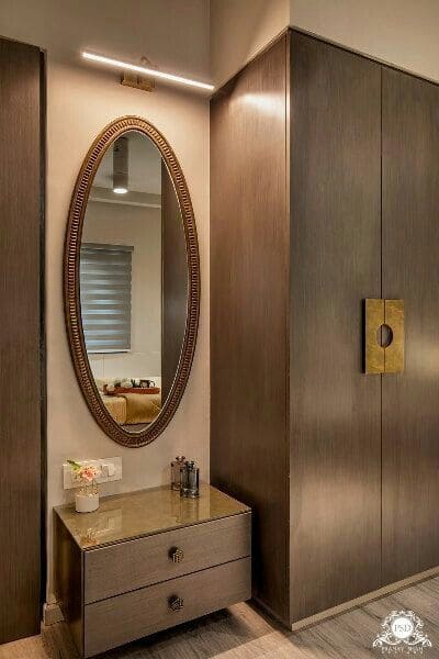Elegant modern interior dressing area by Olangana Design in Bangalore, featuring an oval mirror, floating vanity, and dark wood wardrobes.