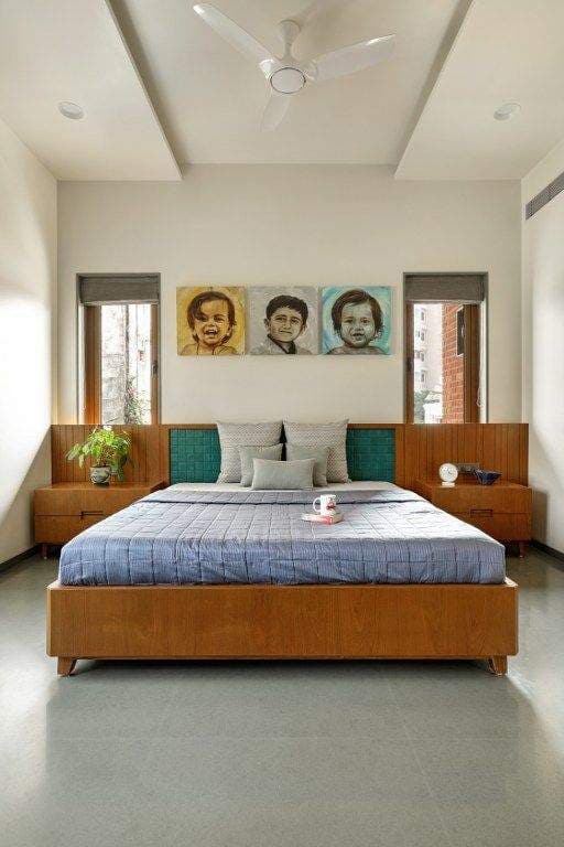 Modern bedroom interior design by Olangana Design in Bangalore featuring a wooden bed, teal upholstered headboard, custom bedside tables, and personalized portraits, creating a serene and inviting space.