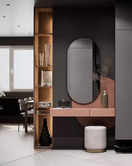 Modern interior design by Olangana Design in Bangalore, featuring a stylish pink vanity with an oval mirror, a white stool, and a tall wooden display shelf with decor.