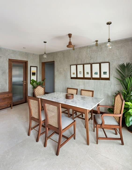Modern dining room interior by Olangana Design in Bangalore featuring a marble top table, wooden cane chairs, concrete walls, and elegant lighting.