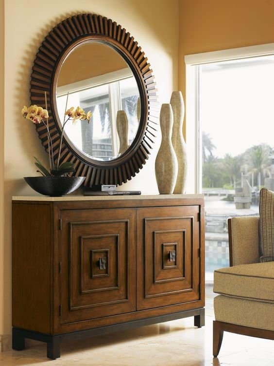 Luxurious entryway interior featuring a wooden console cabinet, ornate circular mirror, and yellow orchids, expertly designed by Olangana Design in Bangalore.
