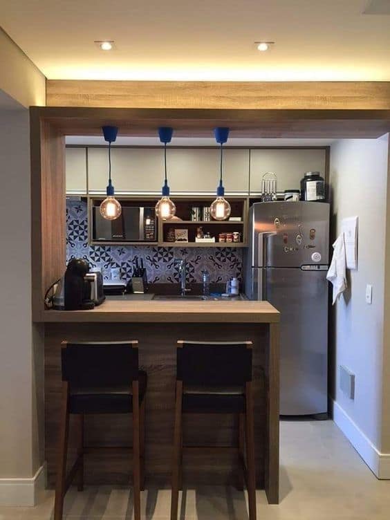 Modern compact kitchen interior with wooden breakfast bar, blue pendant lights, and patterned backsplash designed by Olangana Design in Bangalore.