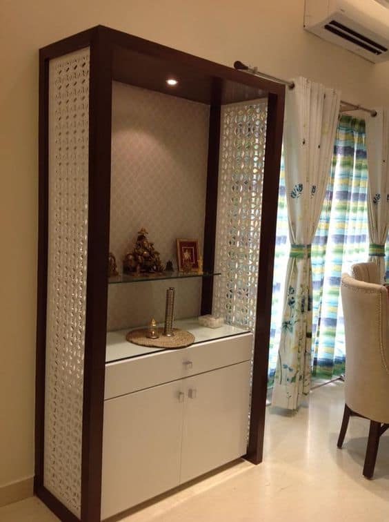 Modern pooja unit interior design by Olangana in Bangalore, featuring a dark wood frame, intricate white jali panels, a glass shelf for idols, and integrated storage.