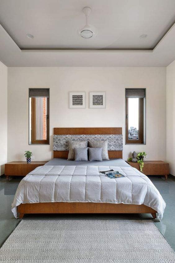 Modern bedroom interior design by Olangana Design in Bangalore featuring a wooden bed, patterned headboard, grey bedding, and minimalist decor.