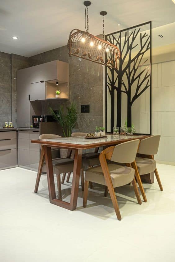 Modern interior dining and kitchen design by Olangana Design in Bangalore, featuring a stylish wooden dining table, unique birdcage chandelier, and elegant tree motif partition.