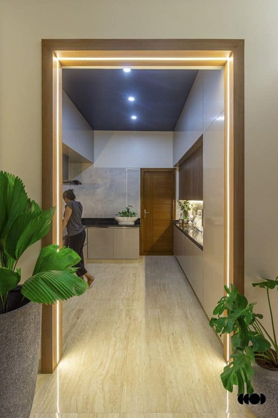 Modern kitchen interior design by Olangana in Bangalore, featuring a striking illuminated wooden archway, sleek handleless cabinets, a dark ceiling with spotlights, and elegant marble flooring.
