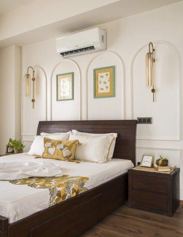 Elegant bedroom interior design by Olangana Design in Bangalore featuring a dark wood bed, white and yellow floral bedding, arched wall decor with gold sconces, and a matching bedside table, showcasing a comfortable and stylish living space.
