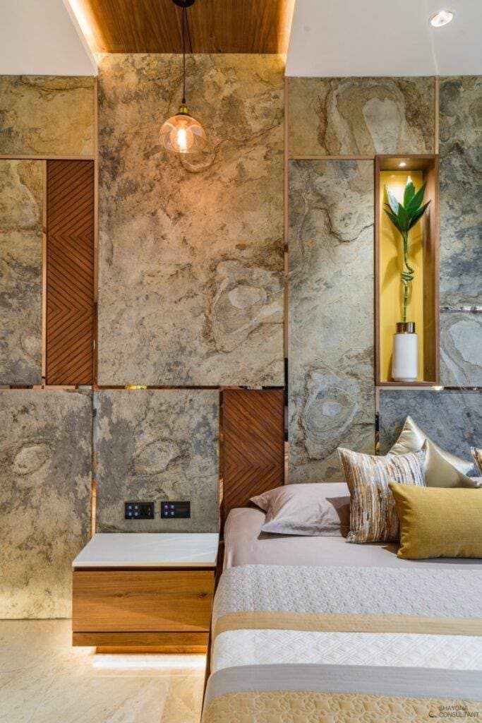 Elegant modern bedroom interior design by Olangana Design in Bangalore, featuring a natural stone accent wall, warm wooden panels, contemporary bedside table, and ambient lighting, creating a luxurious and serene space.