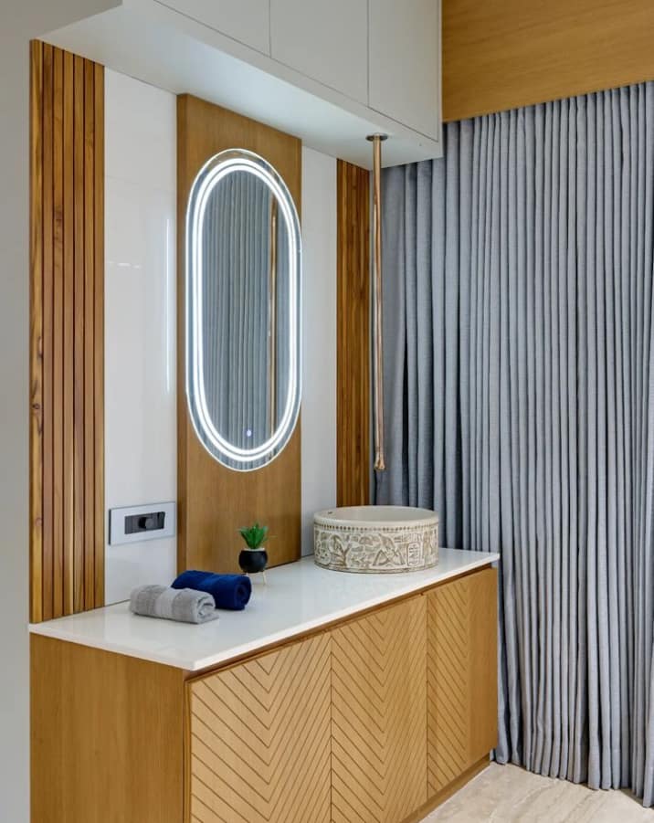 Modern bathroom interior design by Olangana Design in Bangalore featuring a wooden vanity, LED mirror, and ornate basin.