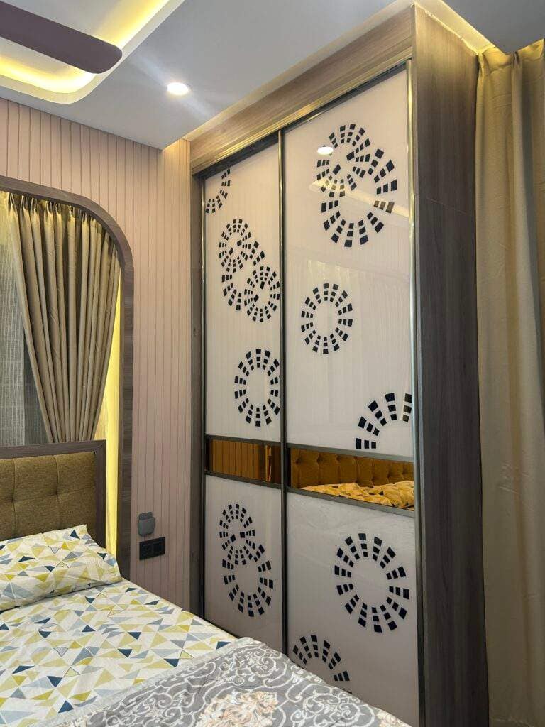 Modern master bedroom interior in a Bangalore apartment featuring a stylish sliding wardrobe with decorative panels, warm lighting, and elegant curtains designed as part of a project by Olangana Design’s.