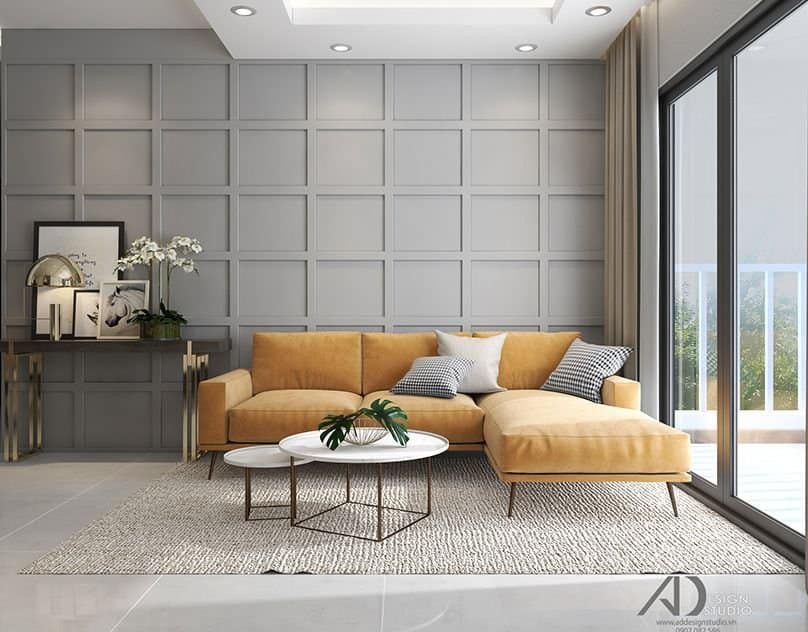 Modern living room interior design by Olangana in Bangalore, showcasing a vibrant mustard yellow sectional sofa, sophisticated grey paneled accent wall, and elegant gold-accented furniture.