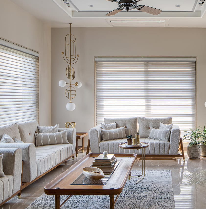 Elegant modern living room interior design by Olangana in Bangalore, featuring neutral-toned sofas, a wooden coffee table, and a striking gold geometric chandelier.