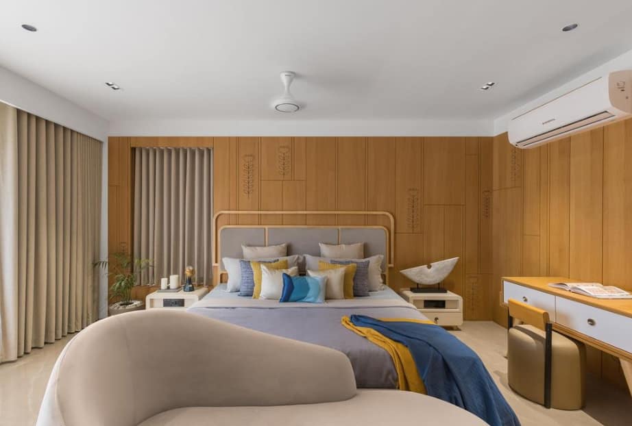 Modern bedroom interior design by Olangana Design in Bangalore featuring a wooden panel accent wall, plush bed with blue and yellow accents, sleek nightstands, and elegant lighting.