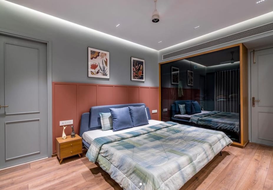 Modern bedroom interior design by Olangana Design in Bangalore, featuring a stylish blue upholstered bed, patterned duvet, terracotta accent wall, and sleek mirrored wardrobe, showcasing elegant residential interior solutions.