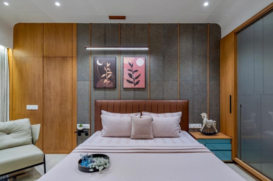 Modern bedroom interior design by Olangana Design in Bangalore featuring a padded headboard, linear pendant light, and textured wall with artistic accents, showcasing expert interior work.