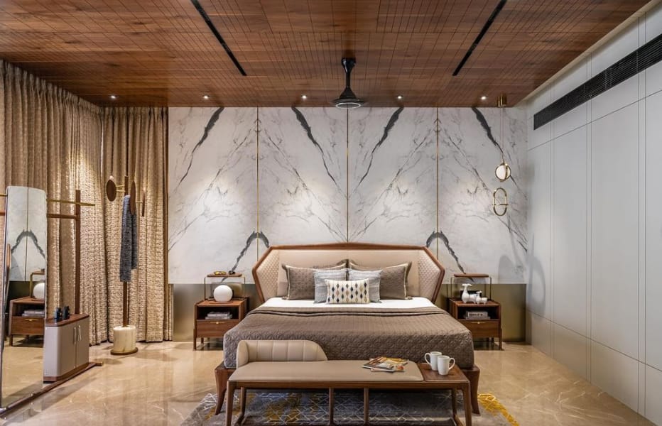 Luxurious contemporary bedroom interior design by Olangana Design in Bangalore, featuring a marble accent wall, wooden ceiling, elegant bed, and bespoke furniture.