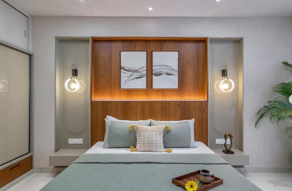 Modern bedroom interior with wooden panel headboard, light green bedding, and elegant wall sconces, designed by Olangana Design in Bangalore.