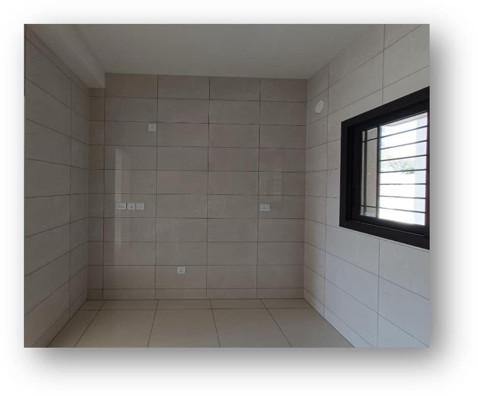 Empty room with light beige tiled walls and floor, black-framed window, and electrical points, a site ready for bespoke interior design transformation by Olangana Design in Bangalore.