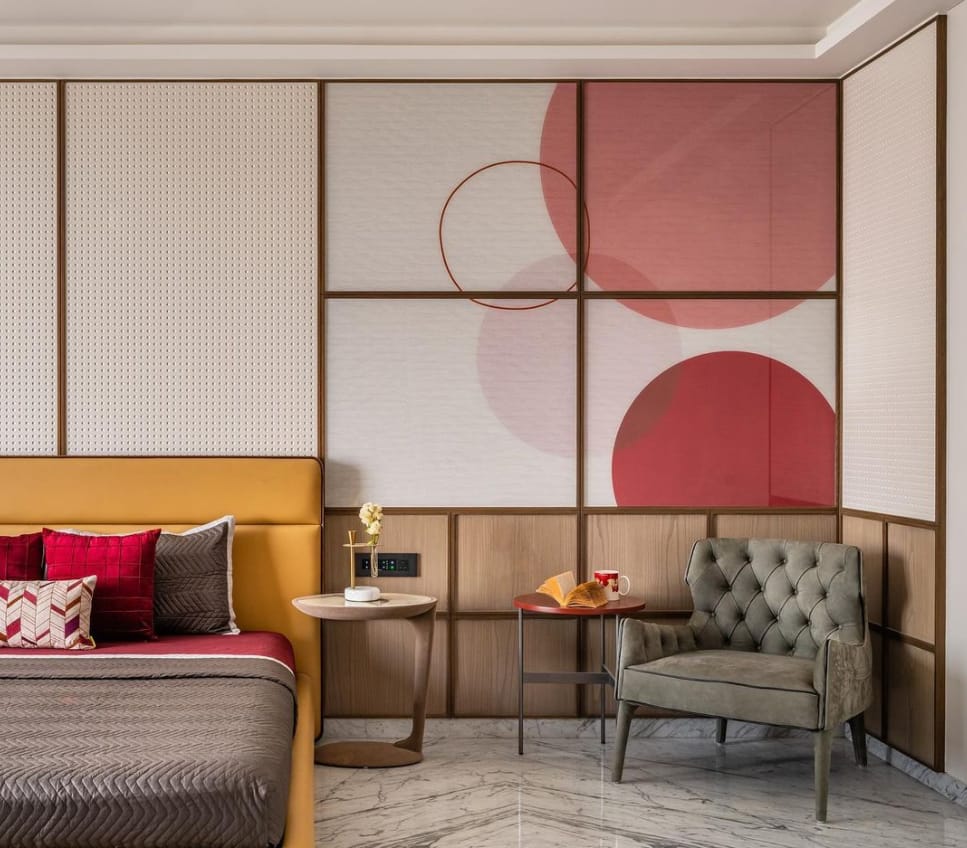 Modern bedroom interior with yellow upholstered bed, red accents, artistic wall paneling, and tufted armchair by Olangana Design in Bangalore. Luxury residential interior design.