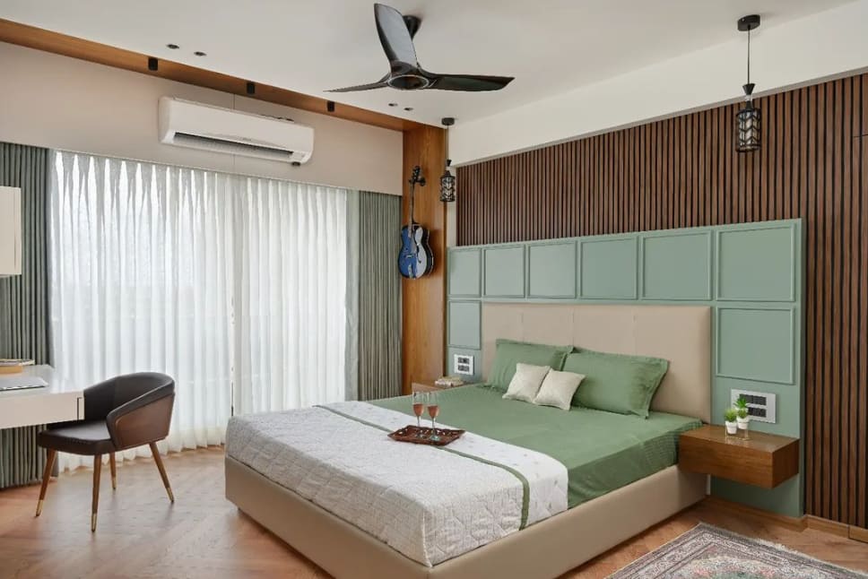 Modern bedroom interior designed by Olangana Design in Bangalore, featuring a green and beige bed, wooden slat accent wall, floating bedside table, and a desk, perfect for contemporary living.