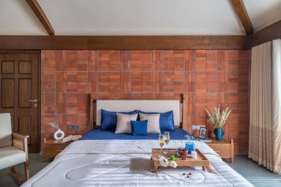 Luxurious bedroom interior by Olangana Design in Bangalore featuring a terracotta brick accent wall, blue bedding, wooden furniture, and elegant decor for a modern aesthetic.