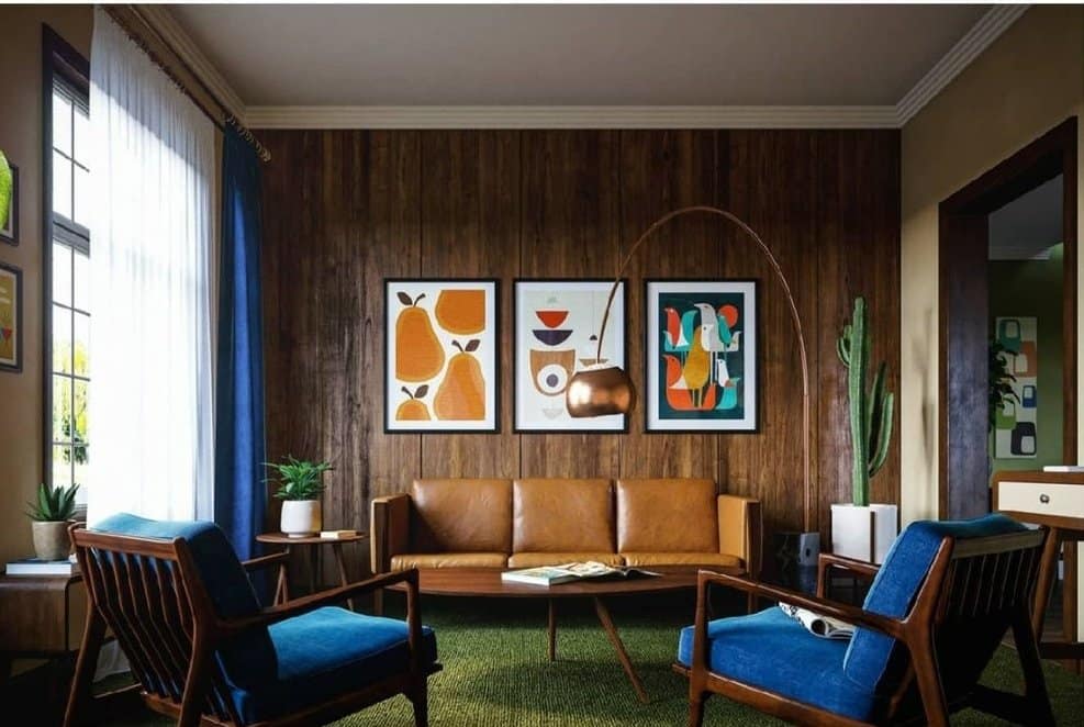 Mid-century modern living room interior design by Olangana in Bangalore, featuring warm wood paneling, a tan leather sofa, blue velvet armchairs, and vibrant abstract art.