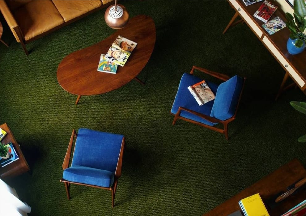 Overhead view of a sophisticated mid-century modern living room interior design by Olangana in Bangalore, featuring a vibrant olive green carpet, a stylish wooden coffee table, and elegant blue upholstered chairs.